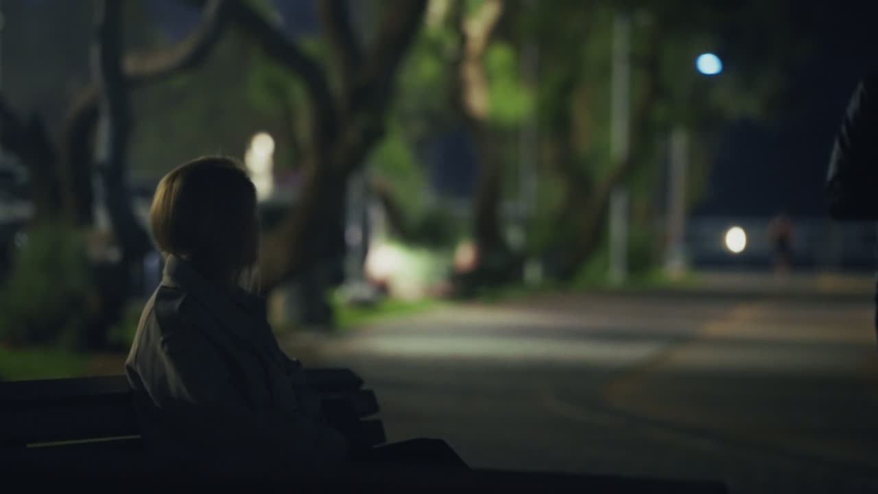 Suspicious package is given to female agent by man in leather jacket in a park. Dark scene at night as two people trade information or pay off debt. Corruption and fraud or conspiracy by government