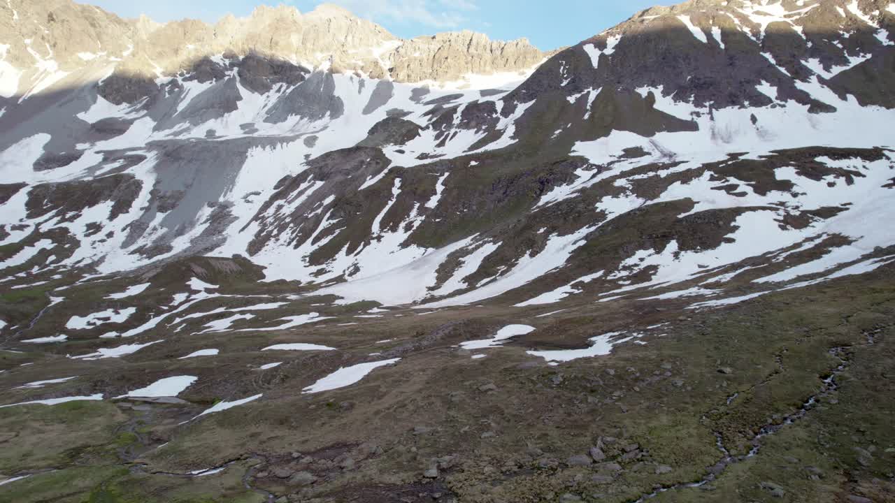 imágenes aéreas de drones que vuelan hacia adelante y giran a través de un espectacular paisaje montañoso irregular con parches residuales de nieve y praderas alpinas para finalmente revelar un valle glacial en suiza