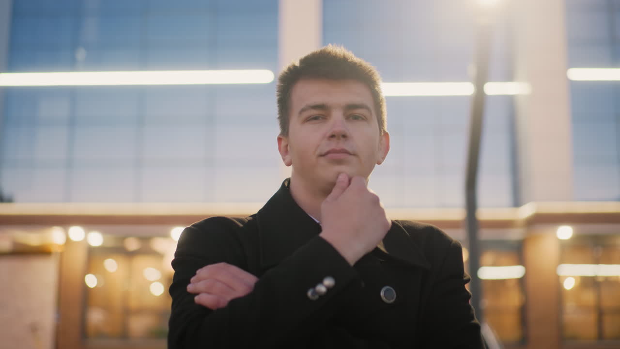 쇼핑몰 앞에서 야외에 서있는 남자가 골든 라이트와 구조를 반사하는 쇼핑몰 유리창으로 도시 환경에서 편안하고 사려 깊은 분위기를 만니다.