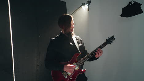 guitarist in black attire passionately plays red electric guitar against stark white backdrop, camera zooming out