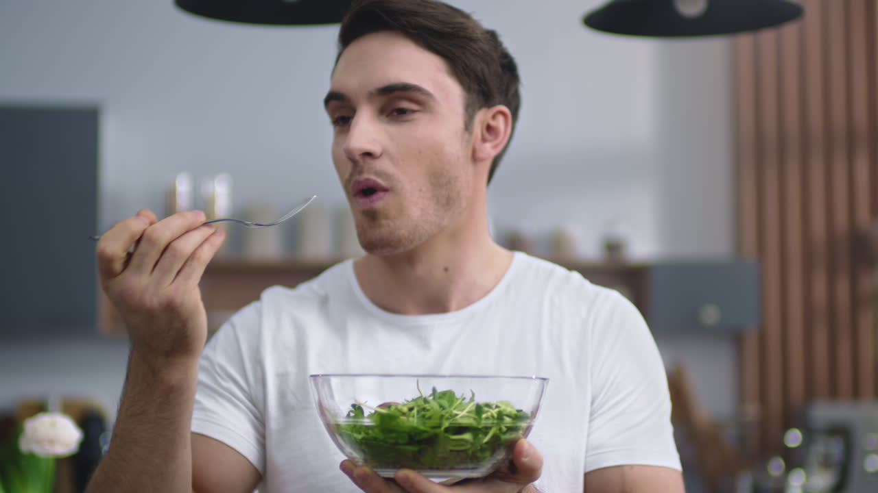 Smiling man eating fresh salad in the kitchen