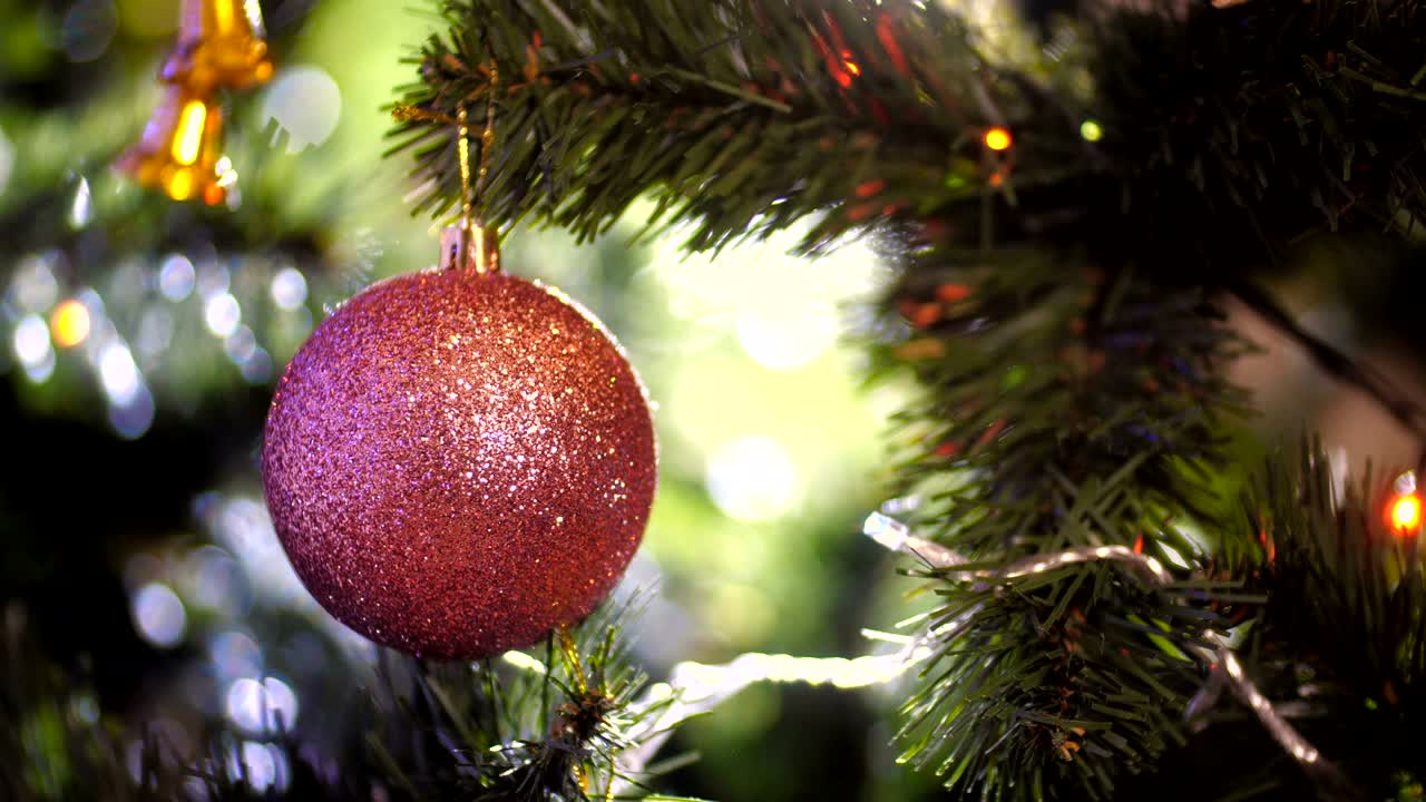 bola de navidad con chispas colgando de un árbol de navidad en un fondo claro de agujas verdes con guirnaldas parpadeantes. primer plano de la decoración de navidad rosa