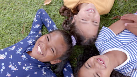 in school, three biracial young girls are lying on grass, heads together