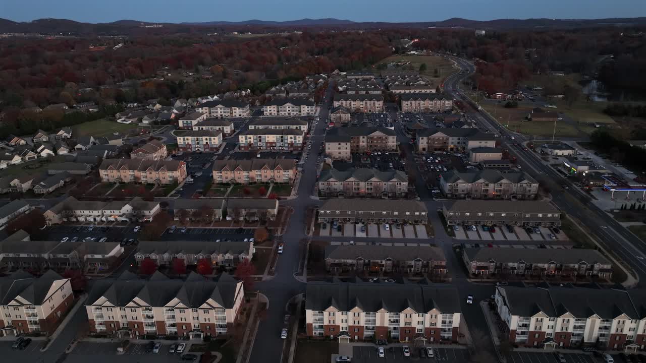 Residential American housing complex at dusk with rows of townhomes, apartments and autumn trees under a fading blue sky, aerial drone wide shot. Calm vibes at sunset