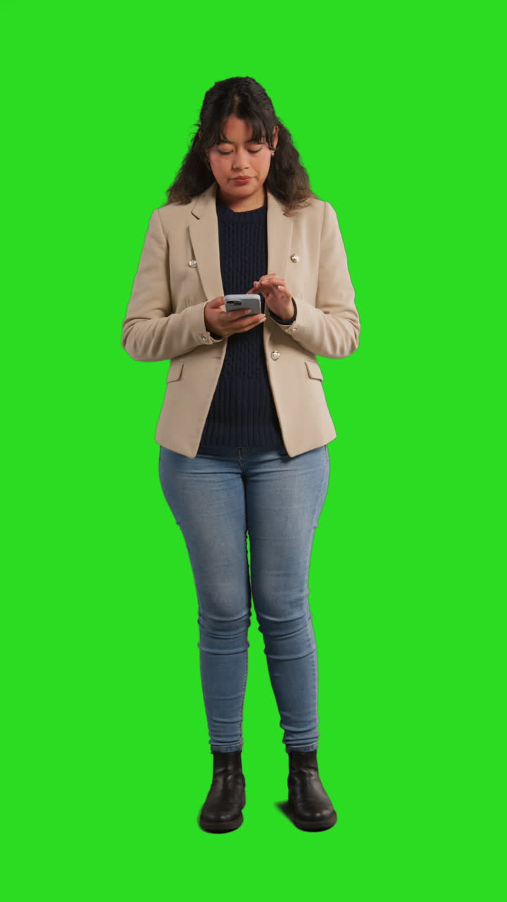 video studio verticale di una donna d'affari che usa il telefono cellulare per inviare messaggi o navigare online in piedi contro lo schermo verde