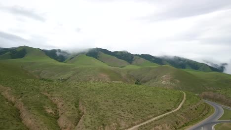 Aerial-panning-shot-across-wide-green-mountain-range-to-road-with-single-car-driving