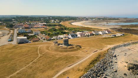 circling drone flight centered around historic martello tower on coastal promontory showing bays and promontory at low tide with boats at anchor and drying on stunning golden beaches