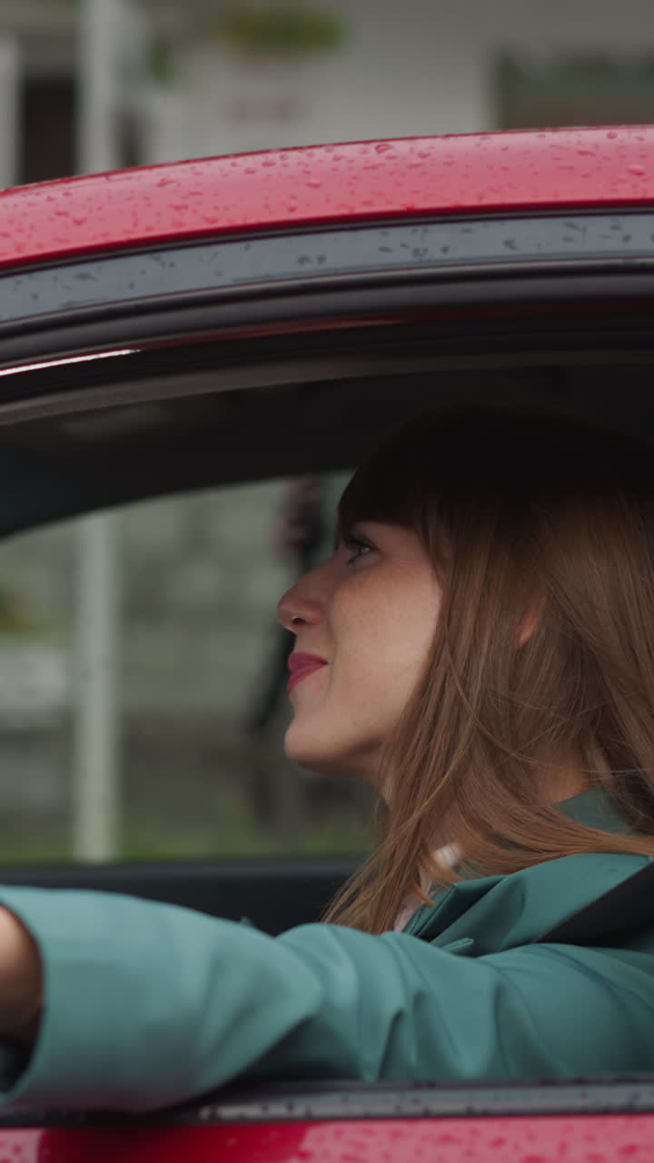 Cheerful woman smiles stretching hand out of car window to feel rain. Happy lady enjoys driving automobile in rainy weather closeup slow motion