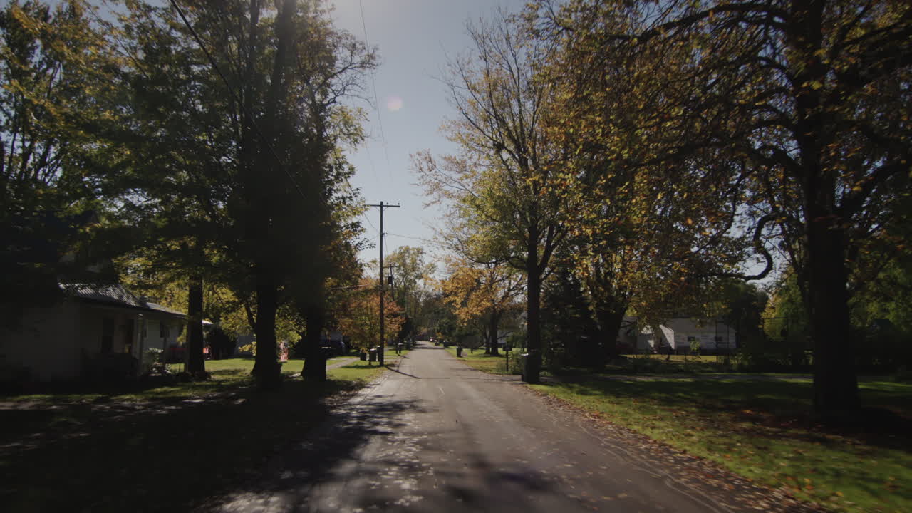 conduce por una calle típica de una ciudad estadounidense en un claro día de otoño. el sol ilumina casas y árboles hermosamente.
