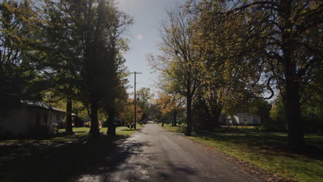 drive along a typical street of an american town on a clear autumn day. the sun illuminates houses and trees beautifully. 4k shot
