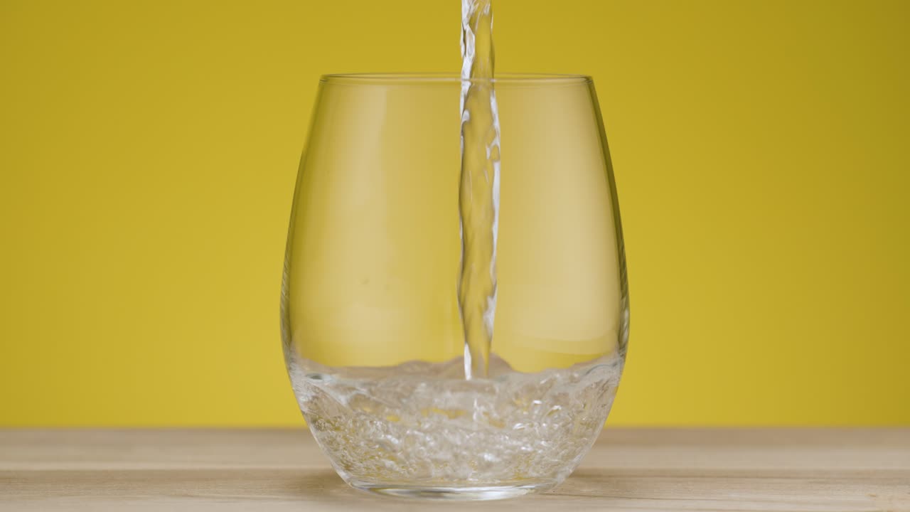 Total shot of a glas filling with sparkling water, isolated yellow backdrop