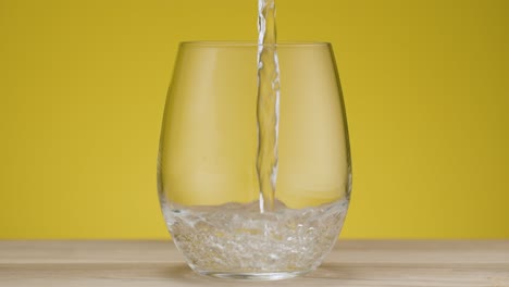 total shot of a glas filling with sparkling water, isolated yellow backdrop