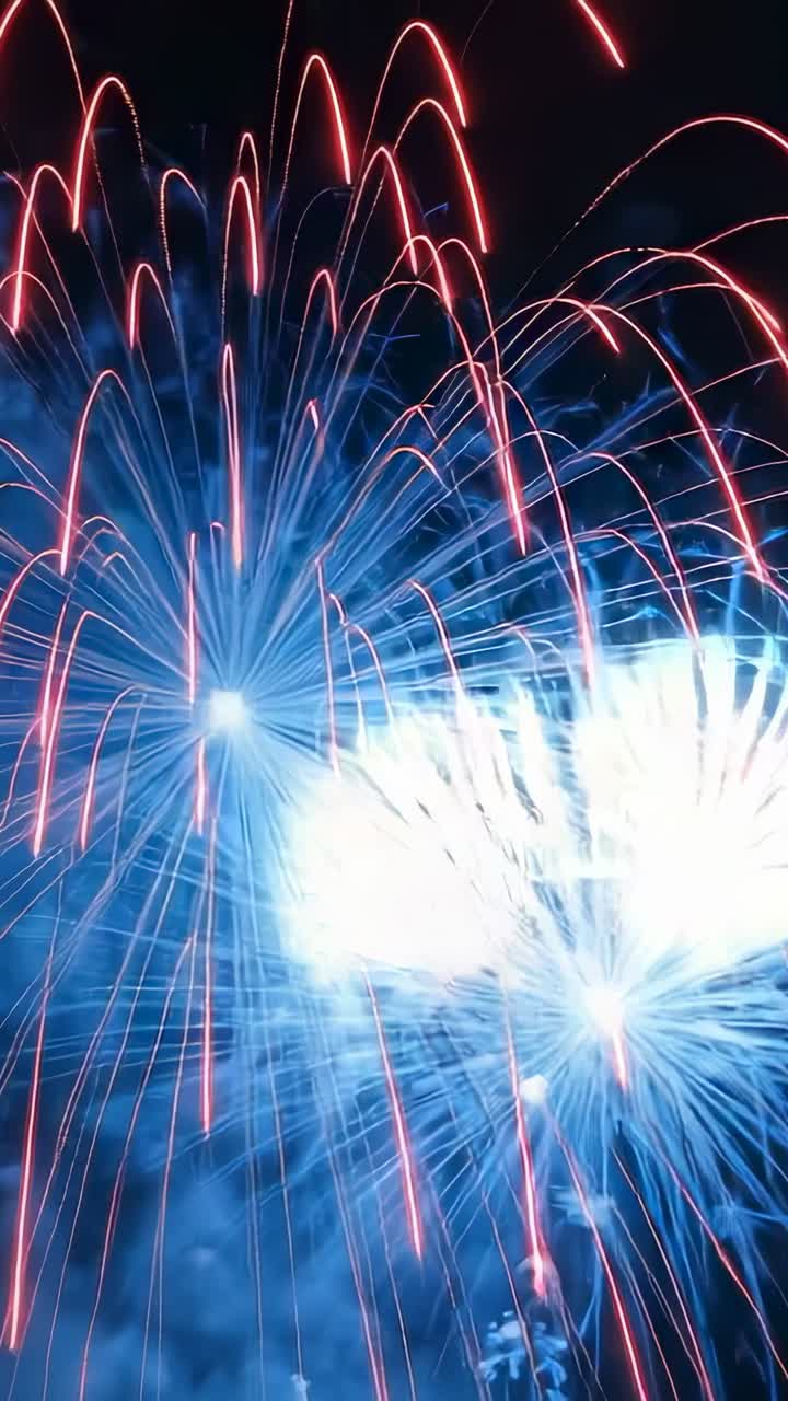 Vertical video: Opening red fireworks bursting into blue pink trails culminating showers at night