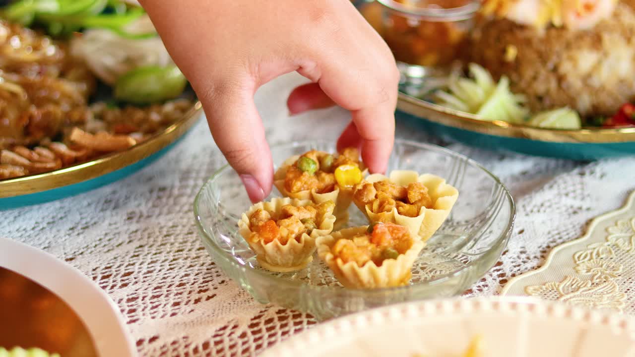 Hands picking Kratong Thong from a plate in a well-lit dining setting, showcasing traditional Thai cuisine in Bangkok