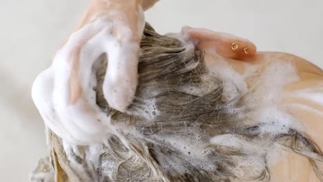 a young woman under a warm stream of shower, she massages the hair of her head with her hands. washing the head with shampoo. care for beautiful long hair. vertical video