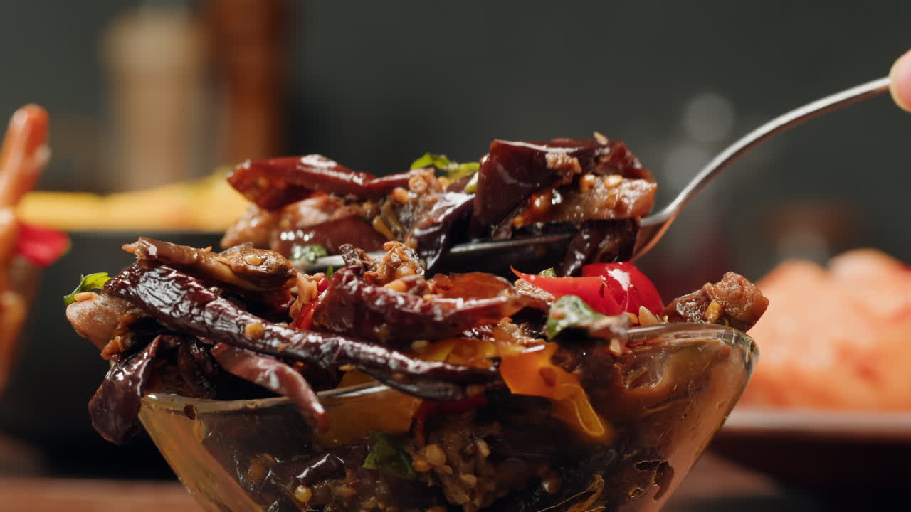 Taking a little bit of fermented eggplants with spices and mustard by spoon close-up. Preservation of vegetables in glass jars. Fermentation preserved aubergine with greens.