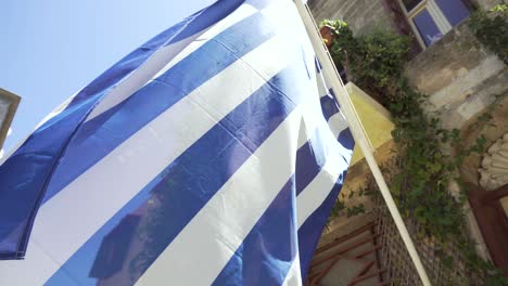 greek national flag waving in front of building on sunny day, close up