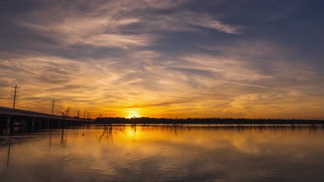 epic stunning timelapse of sunset reflected onto smooth water as cars and boats drive by