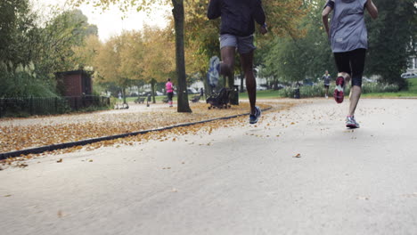 Sportliches-Paar-Läuft-Im-Park-Und-Trägt-Tragbare,-Mit-Technologie-Verbundene-Geräte