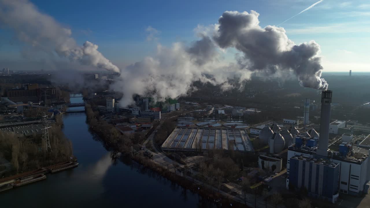 Waste to energy plant emitting smoke from its chimney, located near an urban area, environmental impact of waste. Dramatic aerial view flight drone shot footage from above