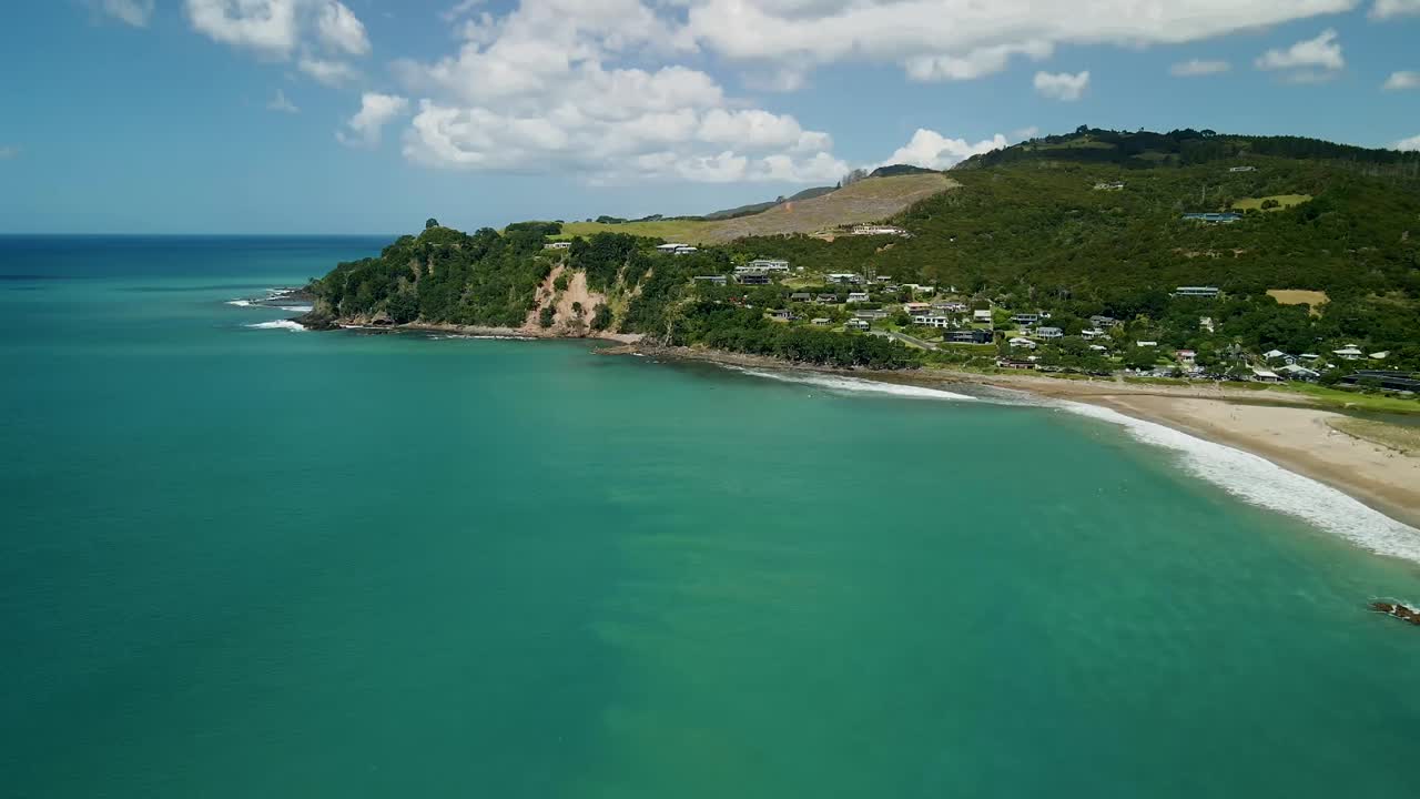 만조 때 바다를 가로지르는 시네마틱 드론 팬, 멀리서 휴식을 취하는 서퍼들과 배경에 있는 산