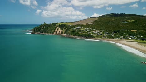 Cinematic-drone-pan-across-water-at-high-tide-with-surfers-catching-the-break-in-the-distance-and-mountains-in-the-background