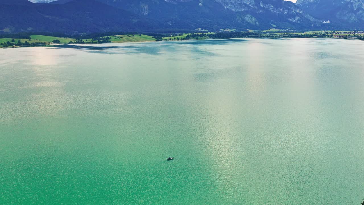 보트가 청록색 물이 있는 큰 호수 위로 운전하고 배경에 알프스 산맥이 드러납니다.