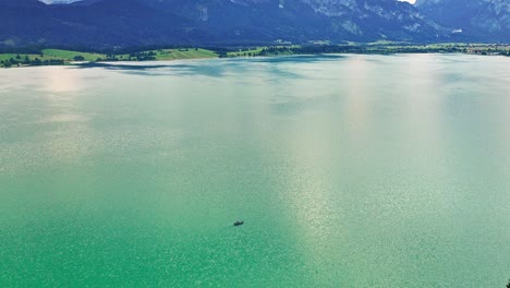 a boat is driving over a big lake with turquiose water and revealing alp mountains in the background