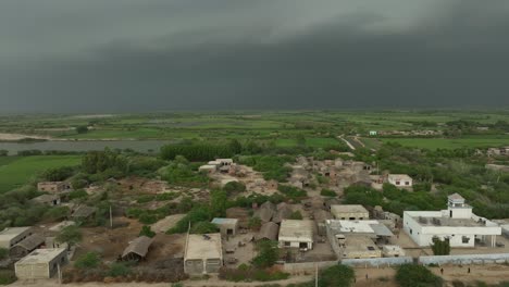 aerial drone rotating shot over rural village houses with green farmlands in the background in mirpurkhas, sindh, pakistan with dark rain clouds at daytime