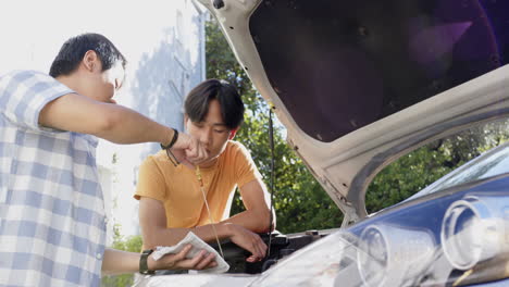 checking car engine oil, asian father and son working together under open car hood