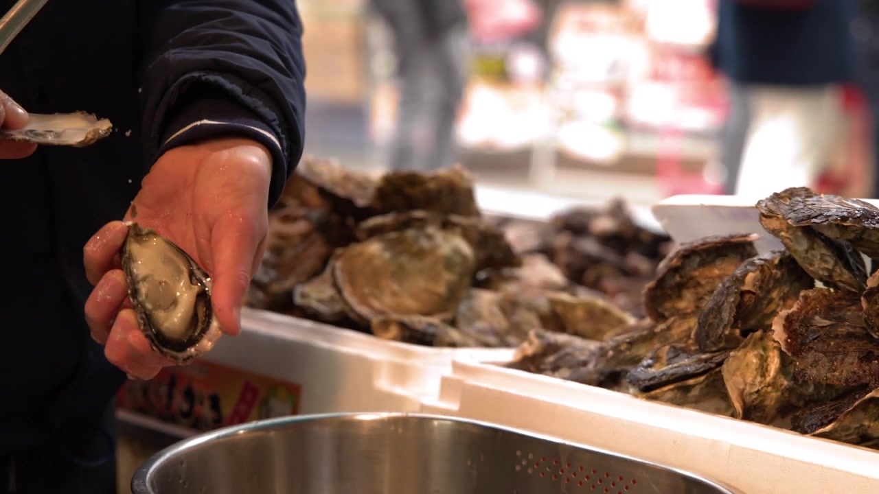 A worker uses a knife to shuck fresh oysters at an outdoor Japanese fish market