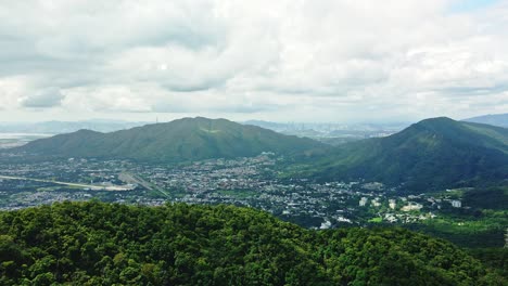 Un-Metraje-Aéreo-Dinámico-Desde-Las-Montañas-Y-Revela-El-Paisaje-Urbano-De-Kam-Tin-En-Hong-Kong-Rodeado-De-Varios-Rascacielos-Y-Hermosas-Formaciones-De-Nubes-Con-El-Buen-Tiempo