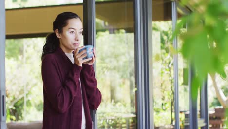 relaxed biracial woman drinking coffee, standing on patio, looking into distance