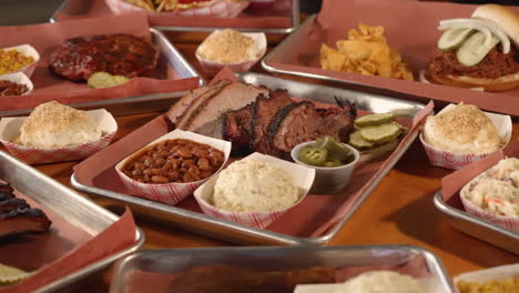 mesa llena de bandejas de barbacoa tradicional de texas, incluyendo pechuga, ensalada de patatas, salchichas, frijoles pintos, costillas, deslizador 4k