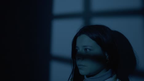 a woman looks thoughtful as she stands in front of her bedroom window after nightfall