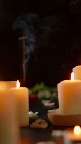 video vertical de vida fija de velas encendidas con pétalos esparcidos incienso palo contra fondo oscuro como parte de la relajante decoración del día de spa 2