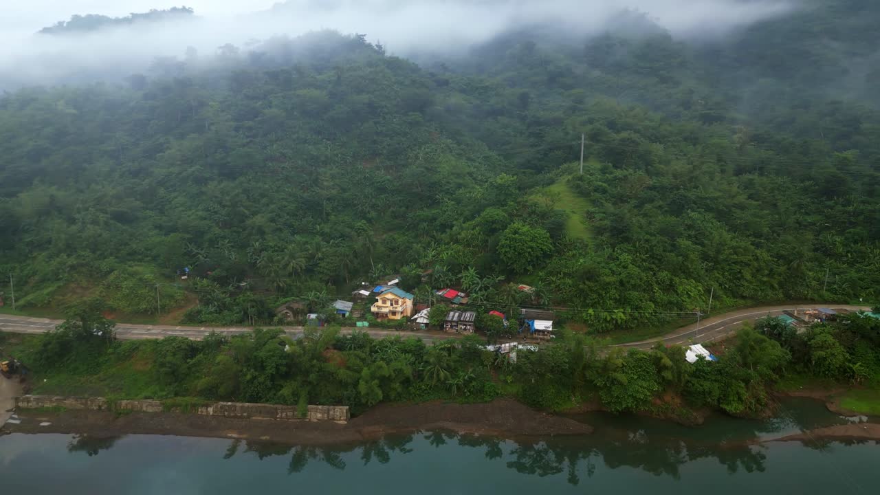 pequeño pueblo en la carretera de la ladera de la montaña junto al río durante la mañana brumosa