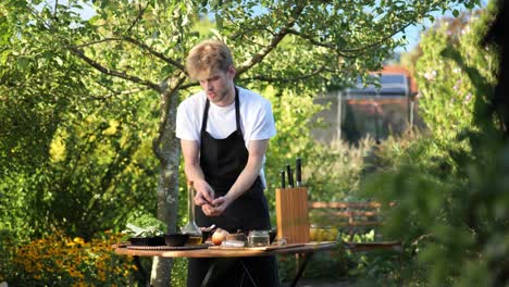 Un-Joven-Preparando-Verduras-Para-Asar-En-Una-Mesa-De-Madera-En-Su-Jardín.