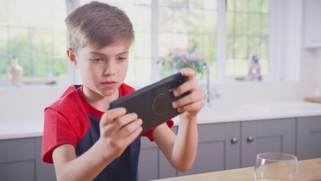 boy at home in kitchen playing game on mobile phone