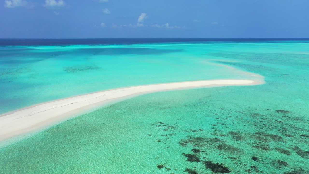 Long narrow sandy stripe surrounded by calm clear water of turquoise lagoon with coral reef on a blue ocean horizon in Maldives