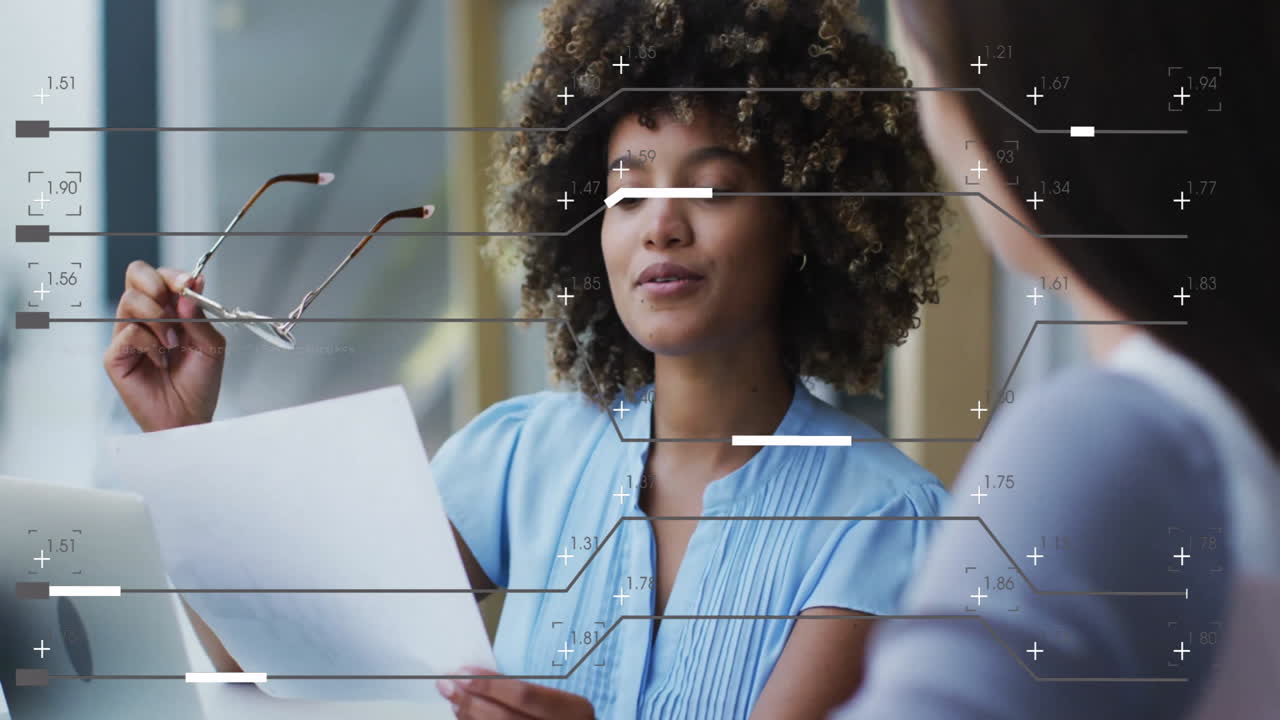 Two female colleagues discussing tech data with laptop in office, showcasing floating data overlay