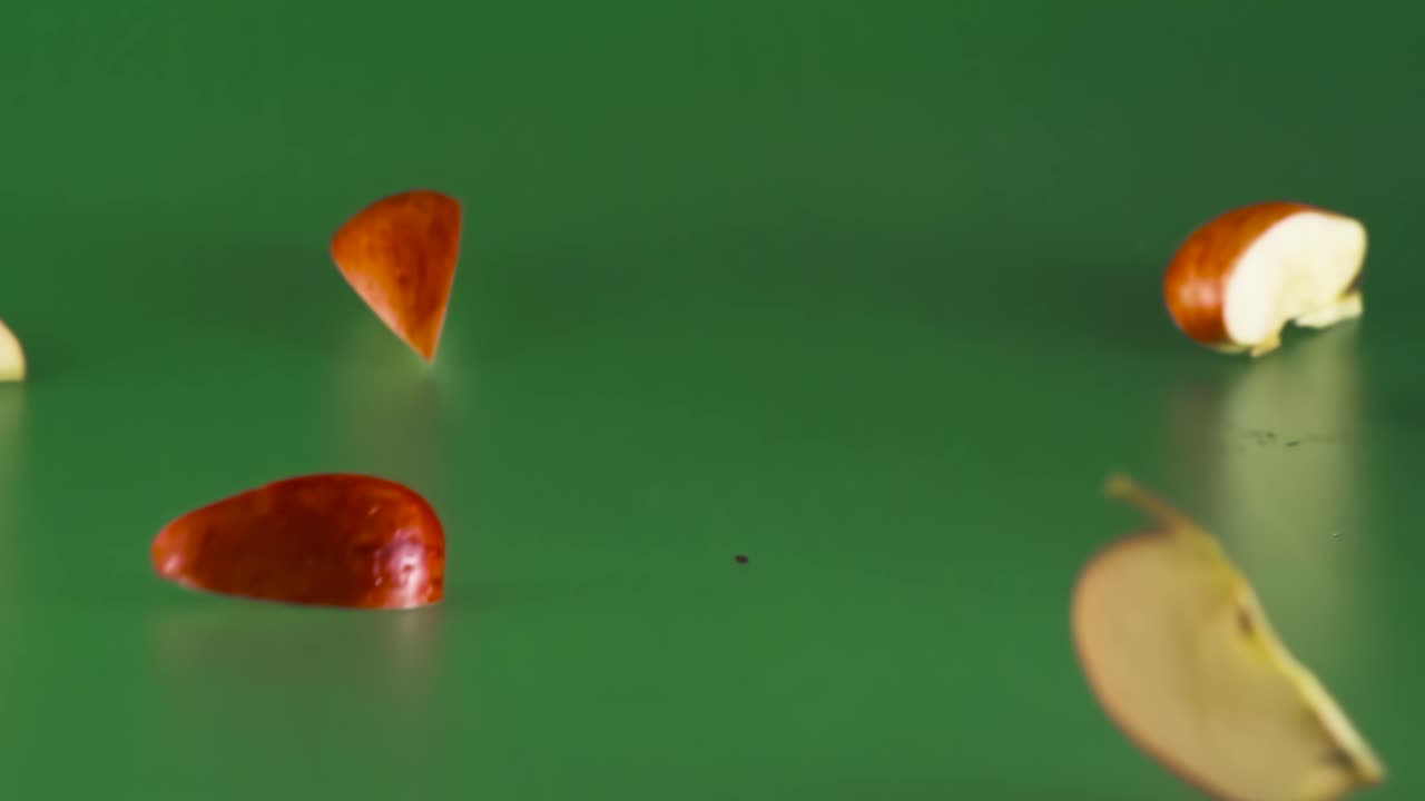 빨간 사과가 떨어지고 녹색 배경에 많은 조각으로 부서집니다.