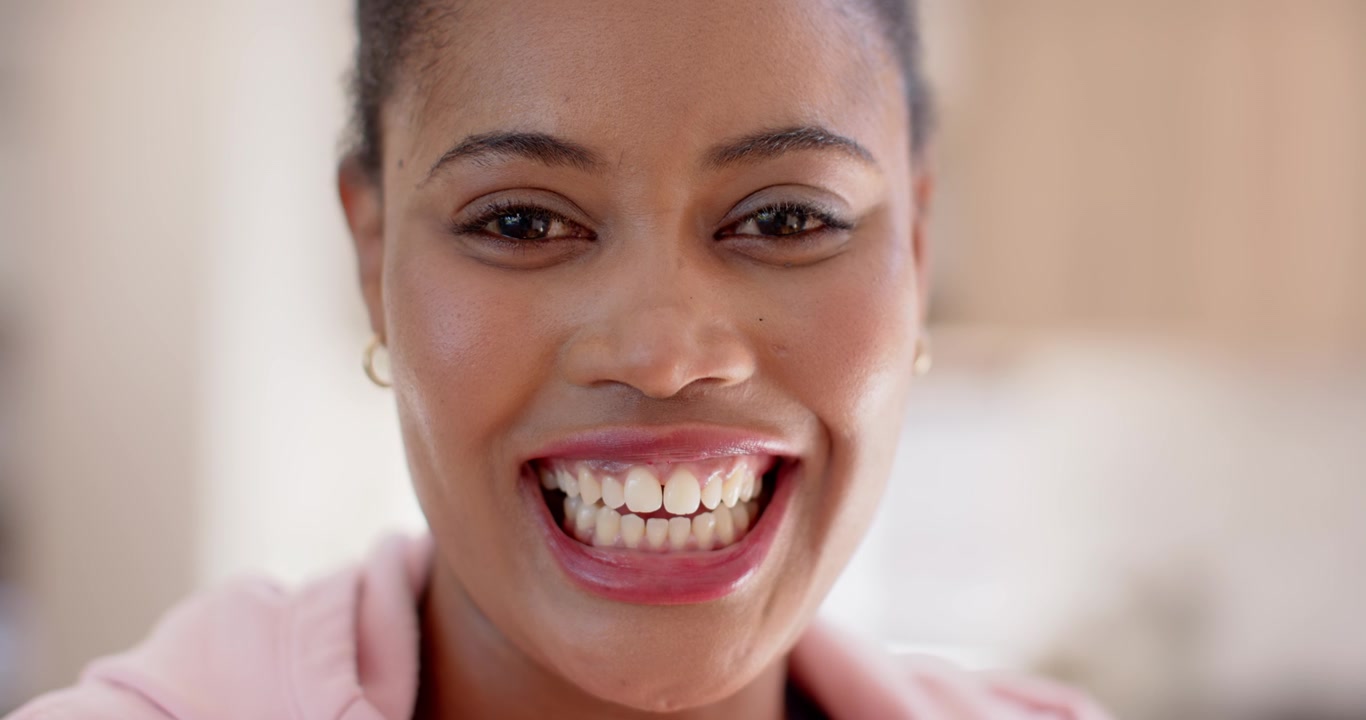 Adult African woman seeing camera smiling laughing teeth showing in kitchen pink hoodie small hoops