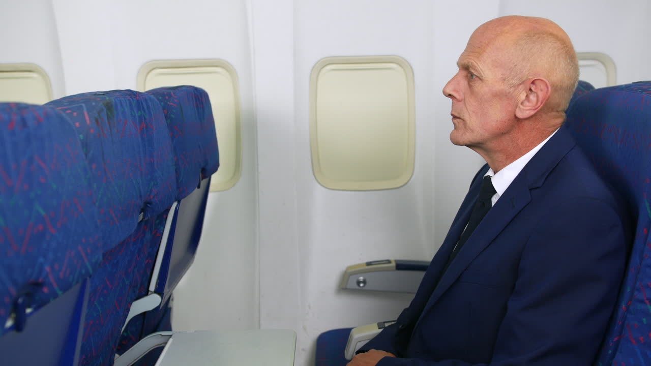 성숙 한 사업가 가 여객기 에 트레이 테이블 을 열고 있다