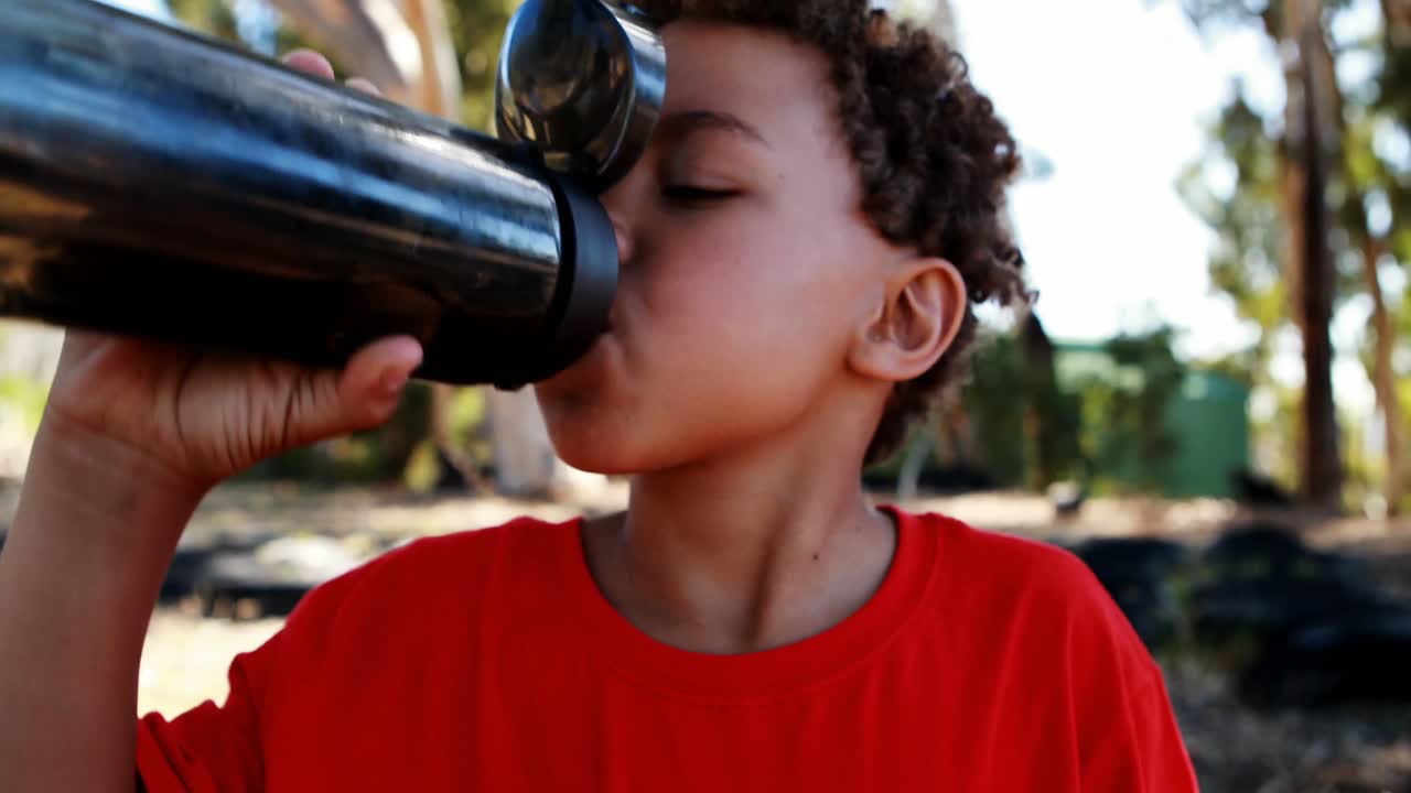 niño deshidratado bebiendo una botella de agua durante una carrera de obstáculos