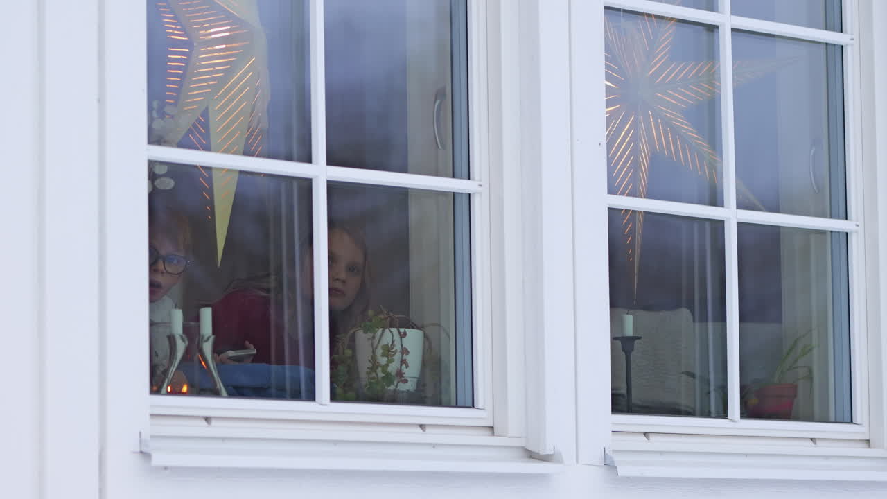 Cute and excited kids at window looking outside waiting for Santa Claus. Static
