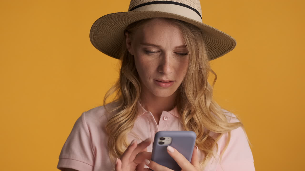 una mujer caucásica con un sombrero enviando mensajes de texto en su teléfono inteligente.