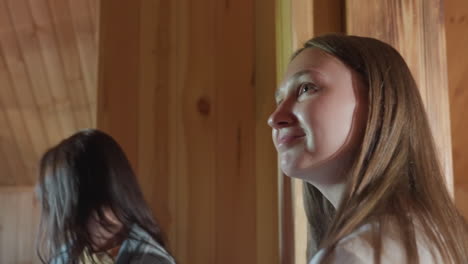 close up of two ladies walking into wooden room with curious expressions, natural light highlighting wood textures and faces, one in denim jacket and other partially visible behind