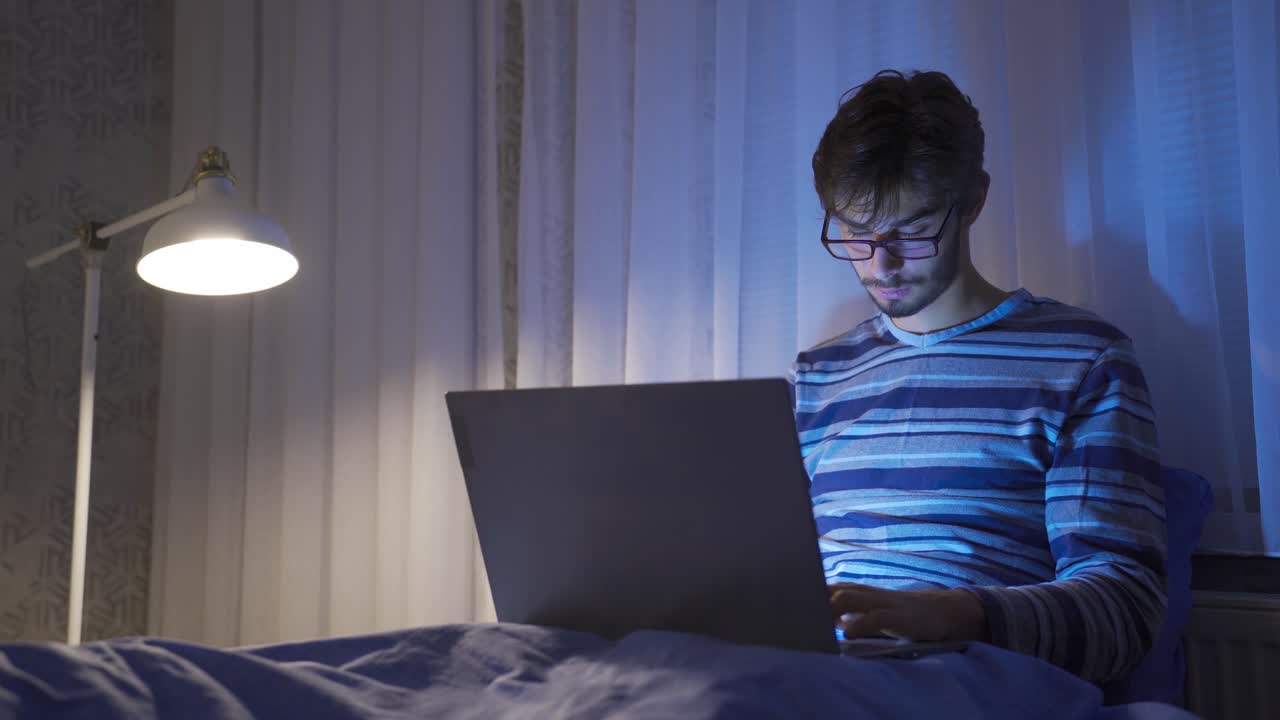 adolescente usando una computadora portátil en la cama, sin dormir y cansado.
