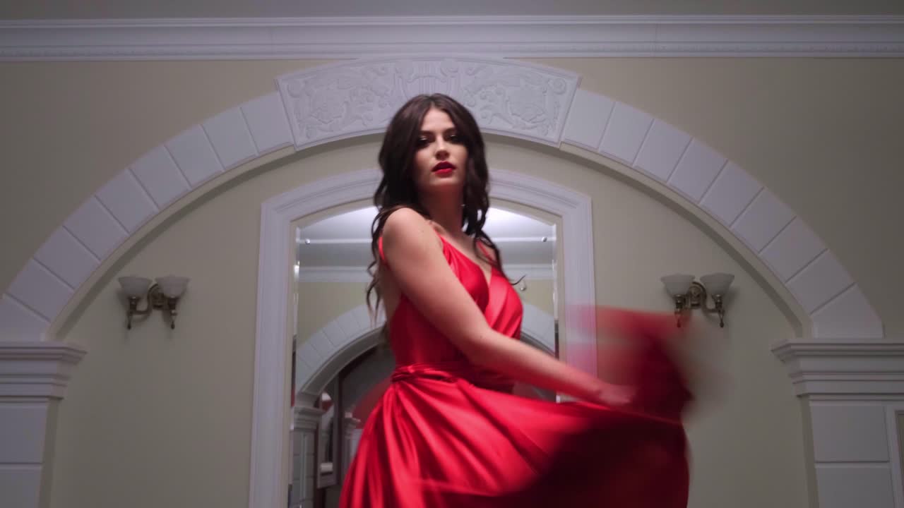 A Captivating Transformation: An Enigmatic Figure in a Flowing Red Gown Appears Gracefully from Shadows into the Light, Embodying Elegance and Poise in a Stunning Indoor Setting